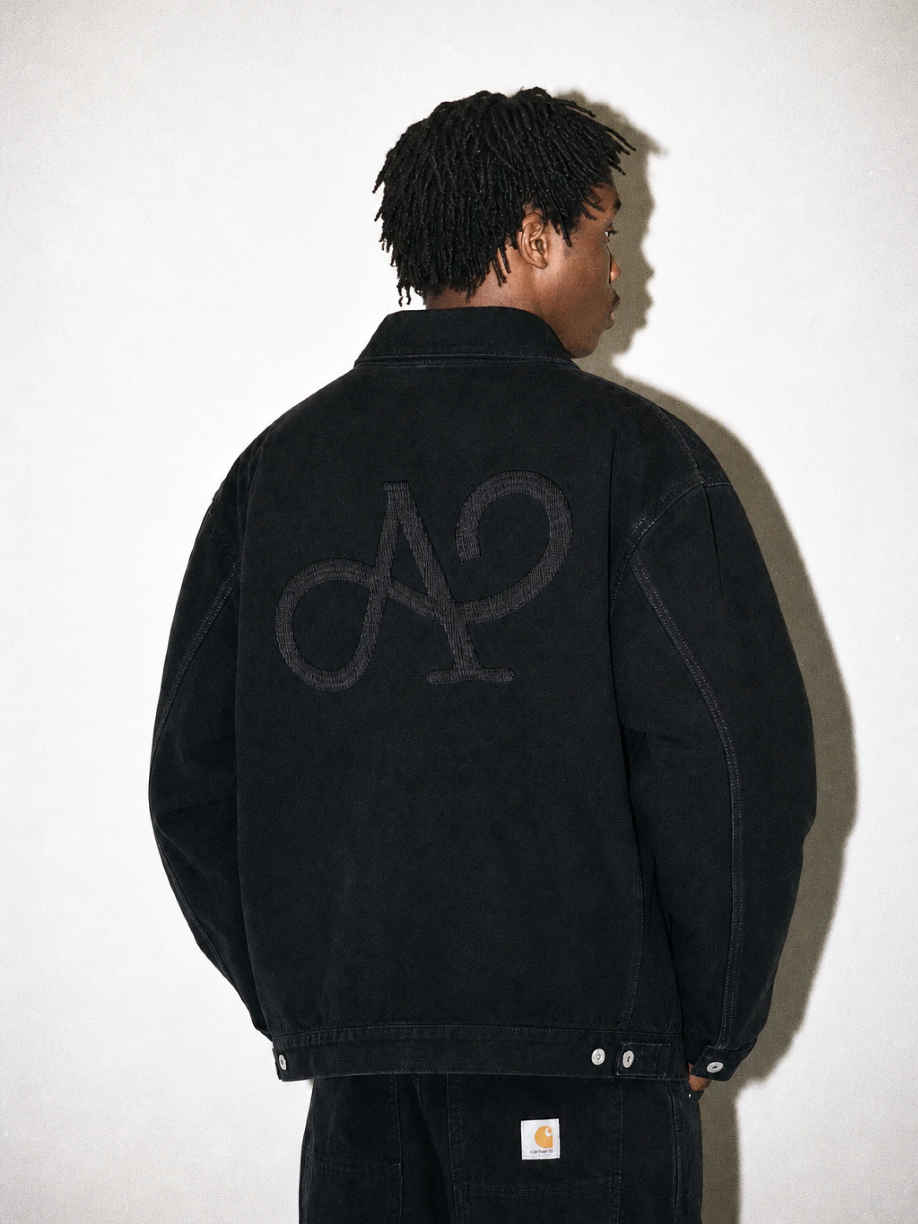 Model in a black denim jacket with a large A monogram on the back